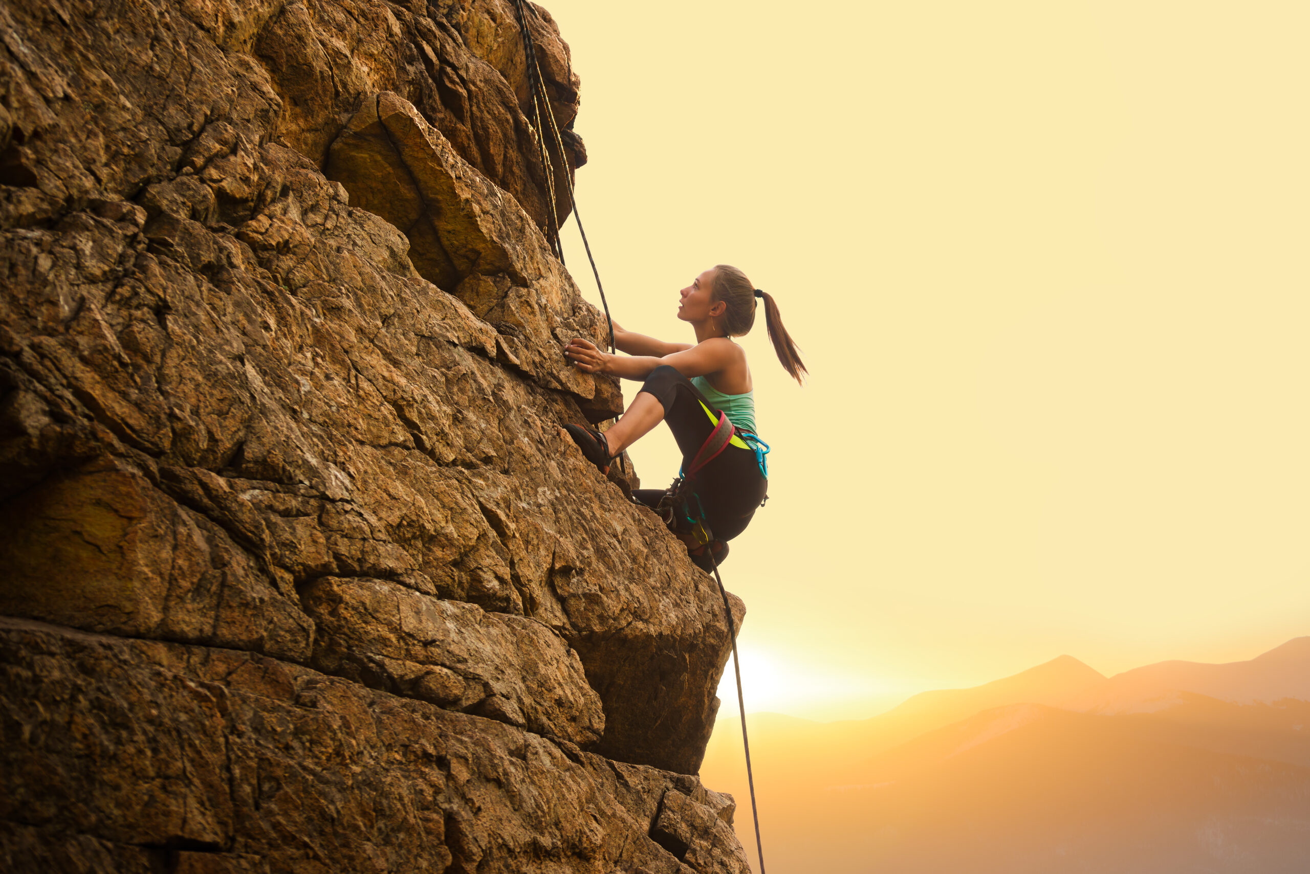 Beautiful,Woman,Climbing,On,The,High,Rock,At,Foggy,Sunset